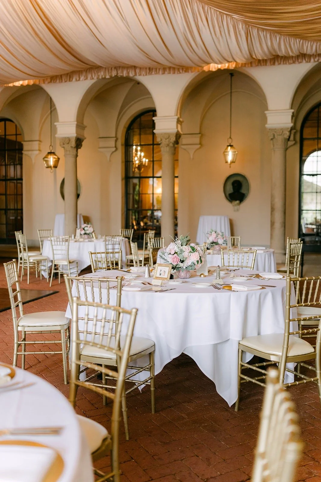 Round tables with white linens and gold chairs set on the West Patio at The Athenaeum