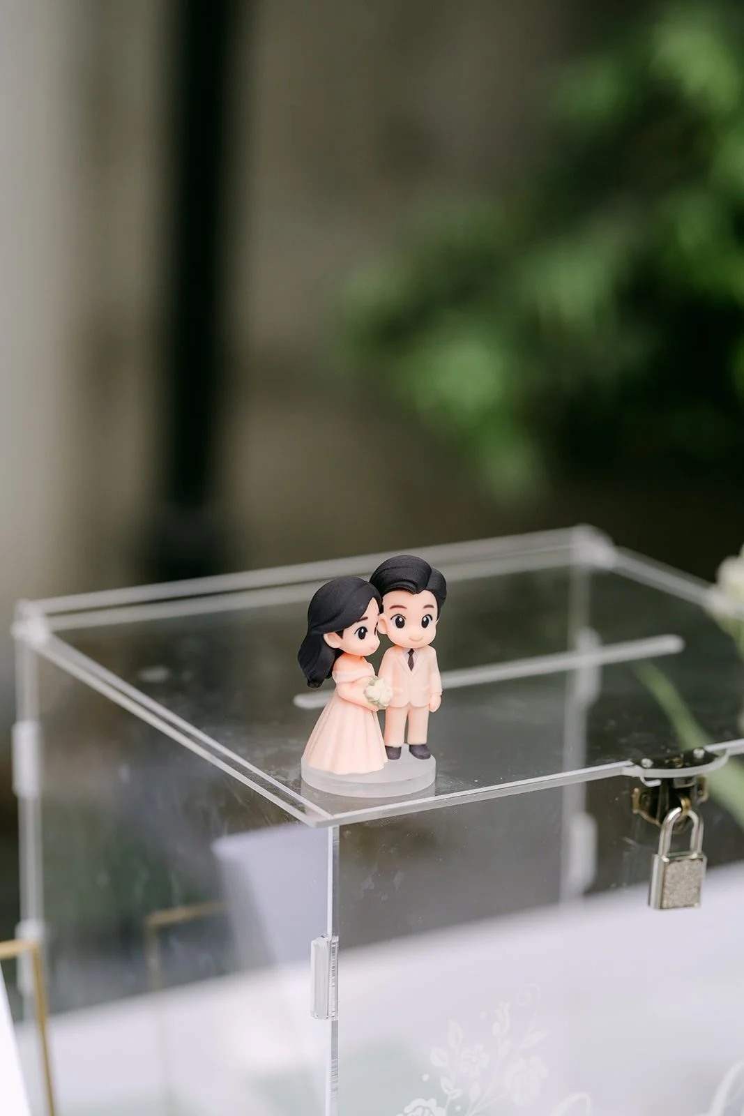 An acrylic card box topped with small figurines of the couple