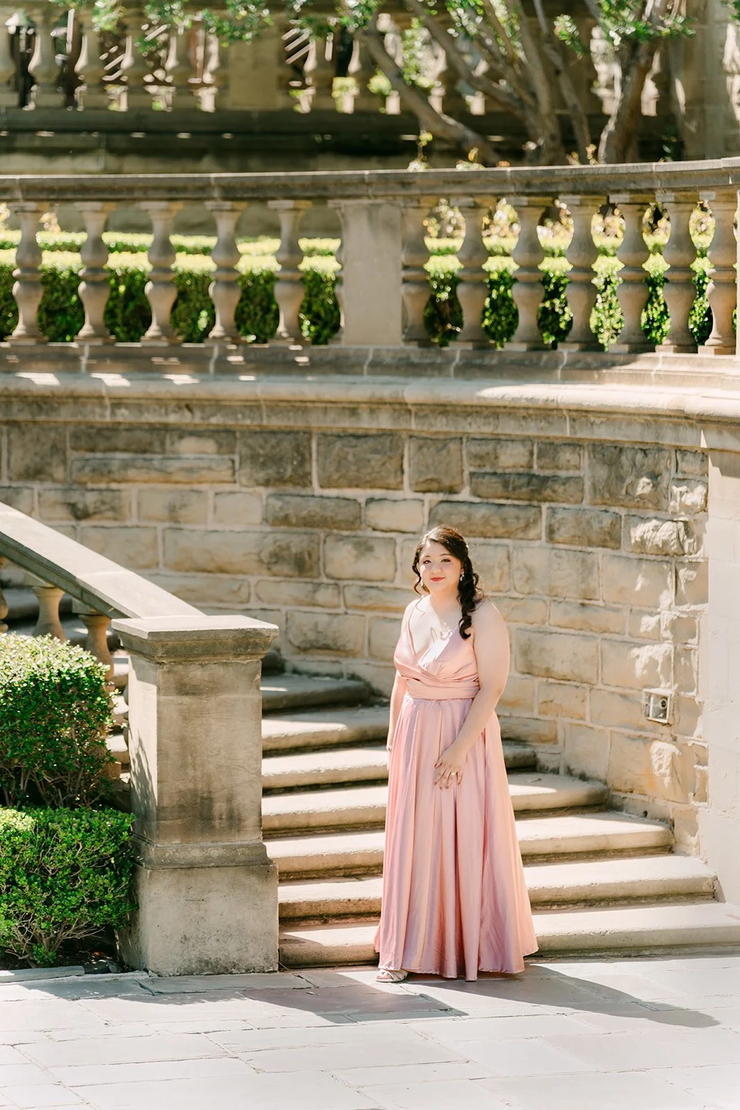 Saira in a blush satin gown at the foot of the stone staircase in Greystone's lower gardens.