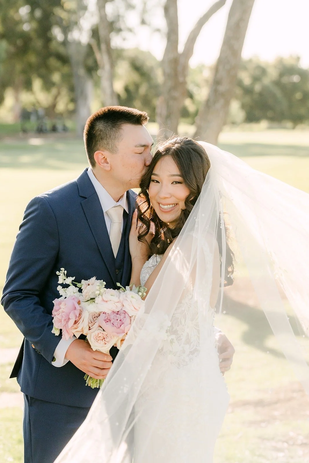 Alex kissing Kelli on the cheek as her veil blows behind them