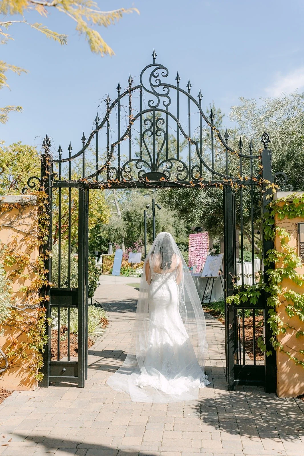 Kelli in her gown and veil framed by the ornate iron gate at Los Robles Greens
