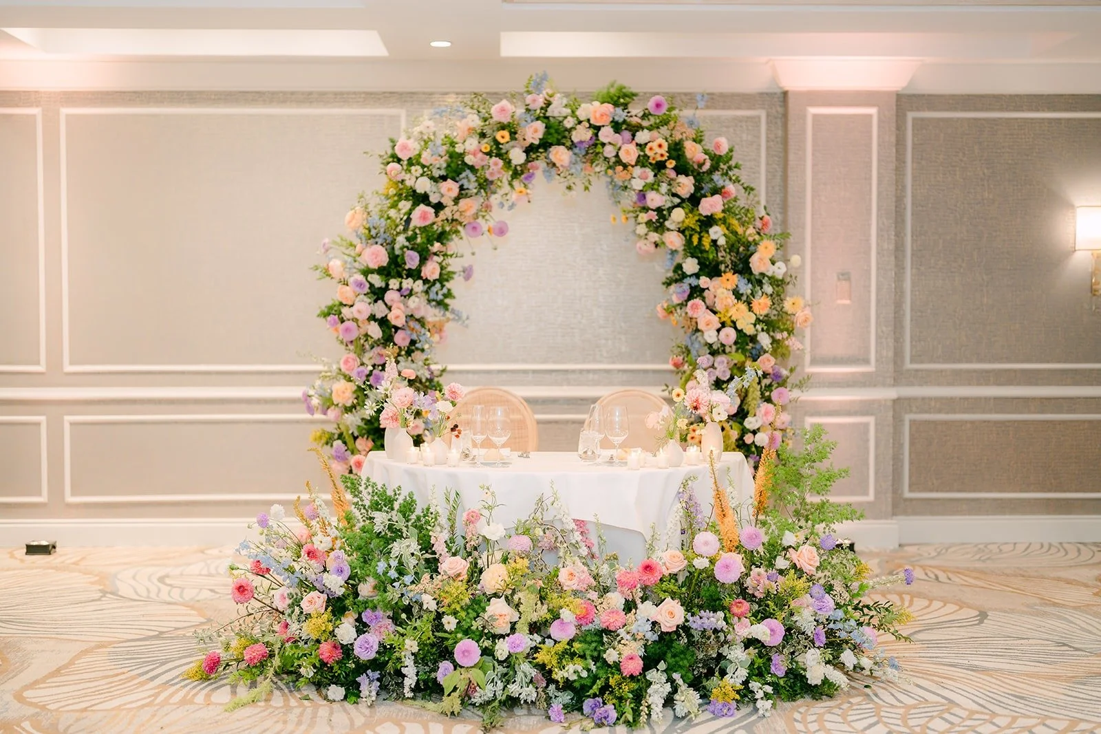 The sweetheart table framed by a floral arch and flowers along the floor