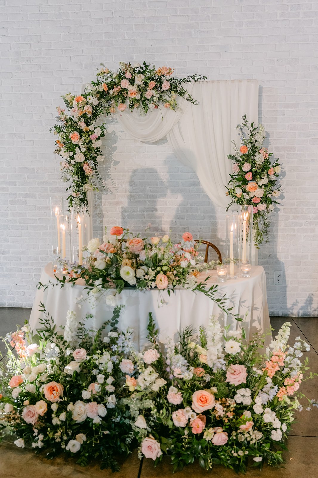 Sweetheart table with a white floral arch and candles at The Colony House