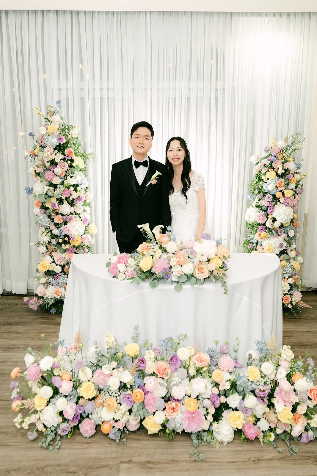 Jeannie and Eunsang at the sweetheart table framed by pastel florals