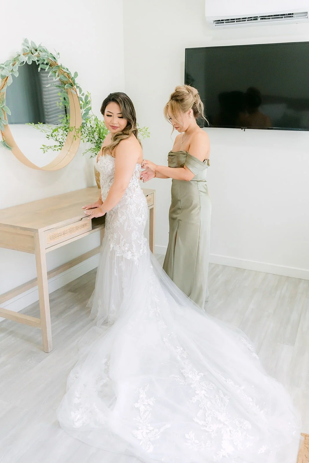 A bridesmaid buttoning Candice's gown at the mirror