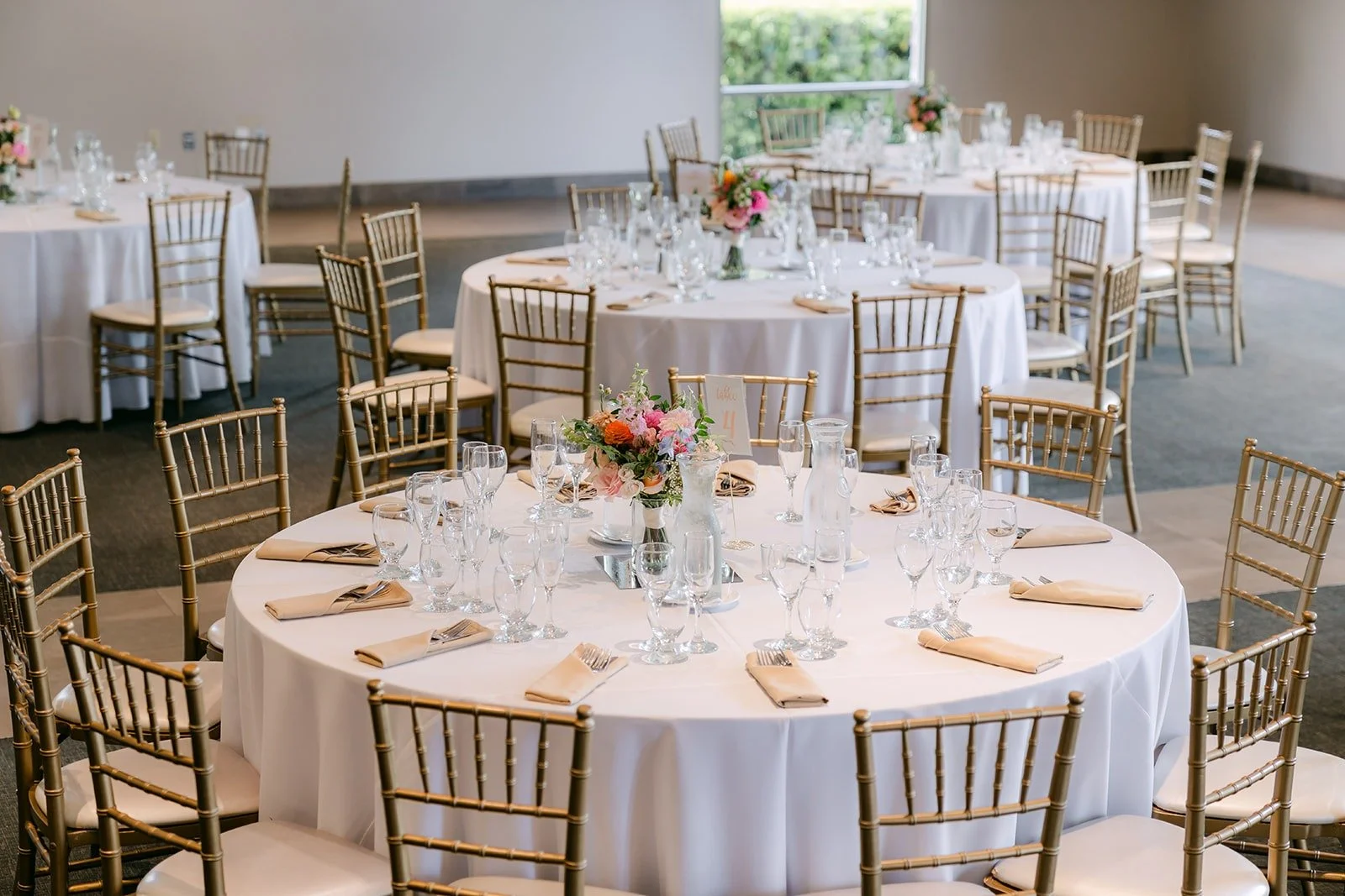 A reception table with a low floral centerpiece and gold chiavari chairs