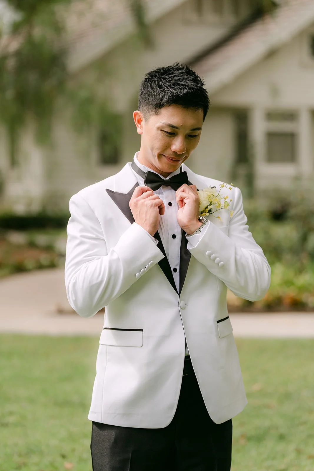 Ryan adjusting his bow tie in his white tuxedo jacket, photographed by One and Only Production.