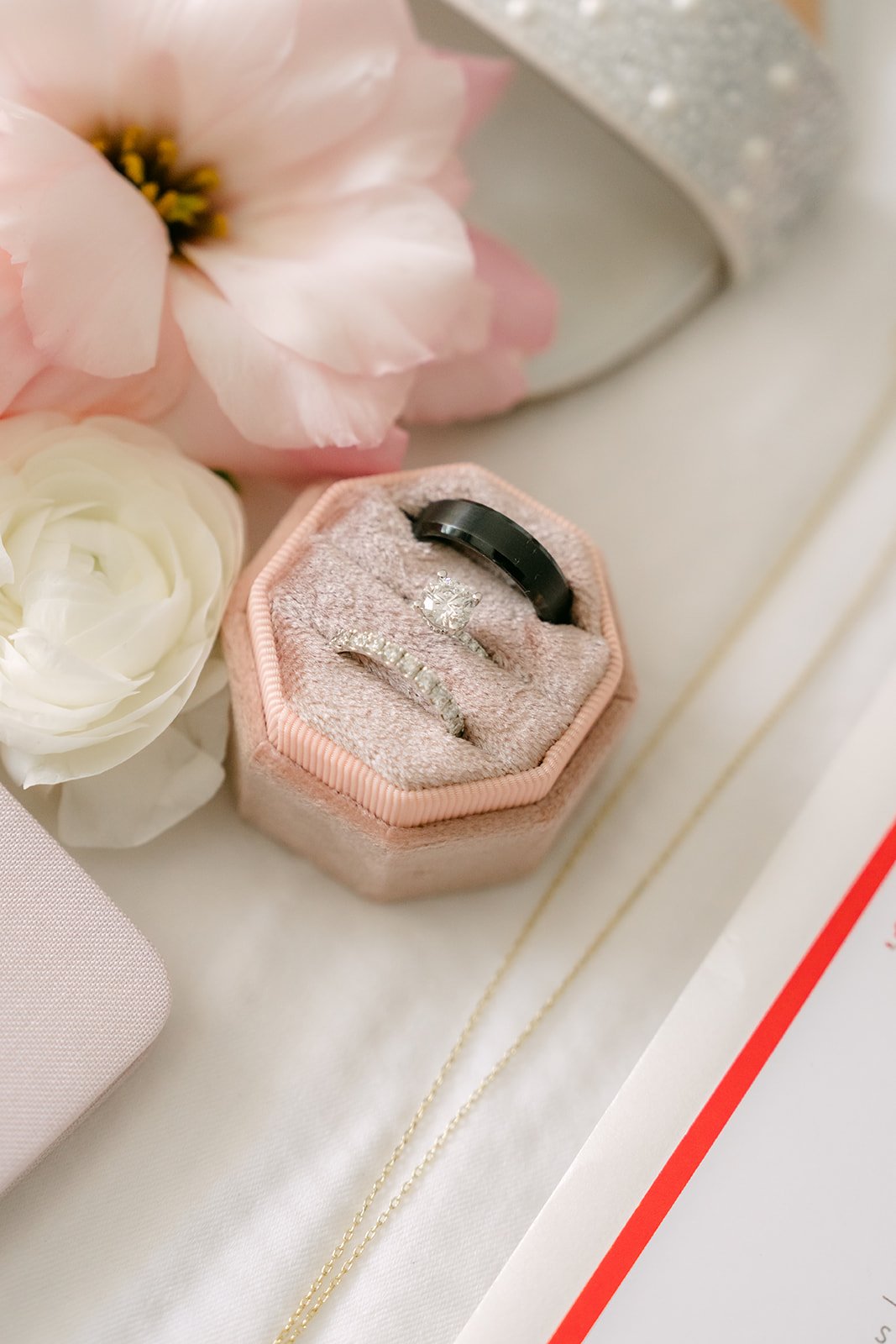 Wedding rings in a pink velvet ring box beside a pink rose.