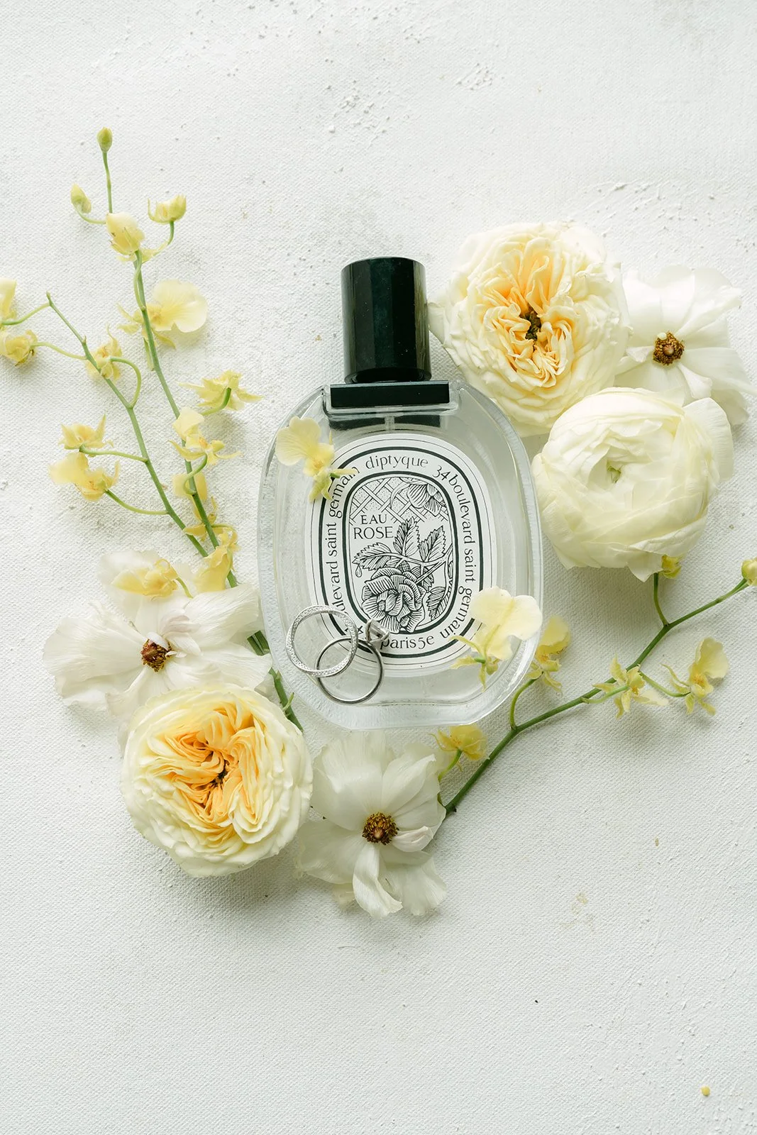 Perfume bottle surrounded by white and butter yellow florals.