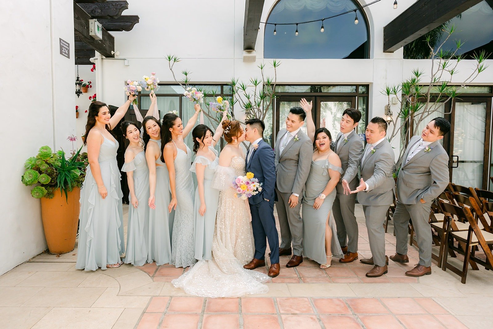 The full wedding party in dusty blue and light gray in the La Ventura courtyard