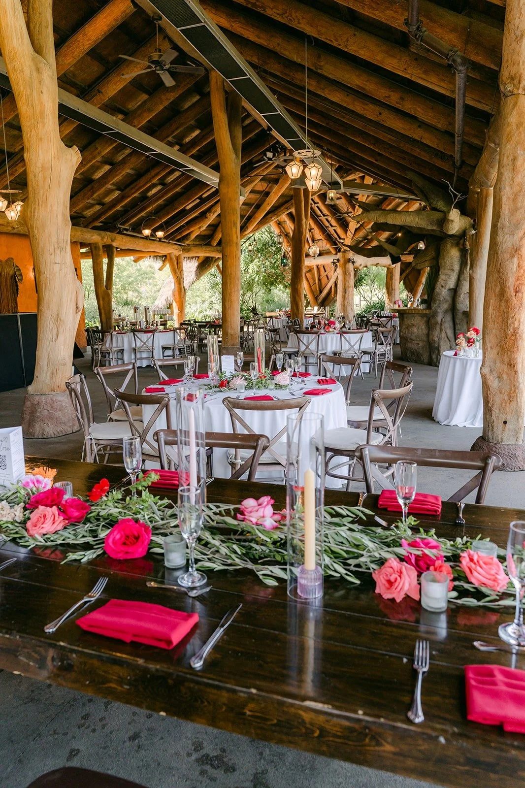 The reception tables under the wooden pavilion with red napkins and pink and red centerpieces
