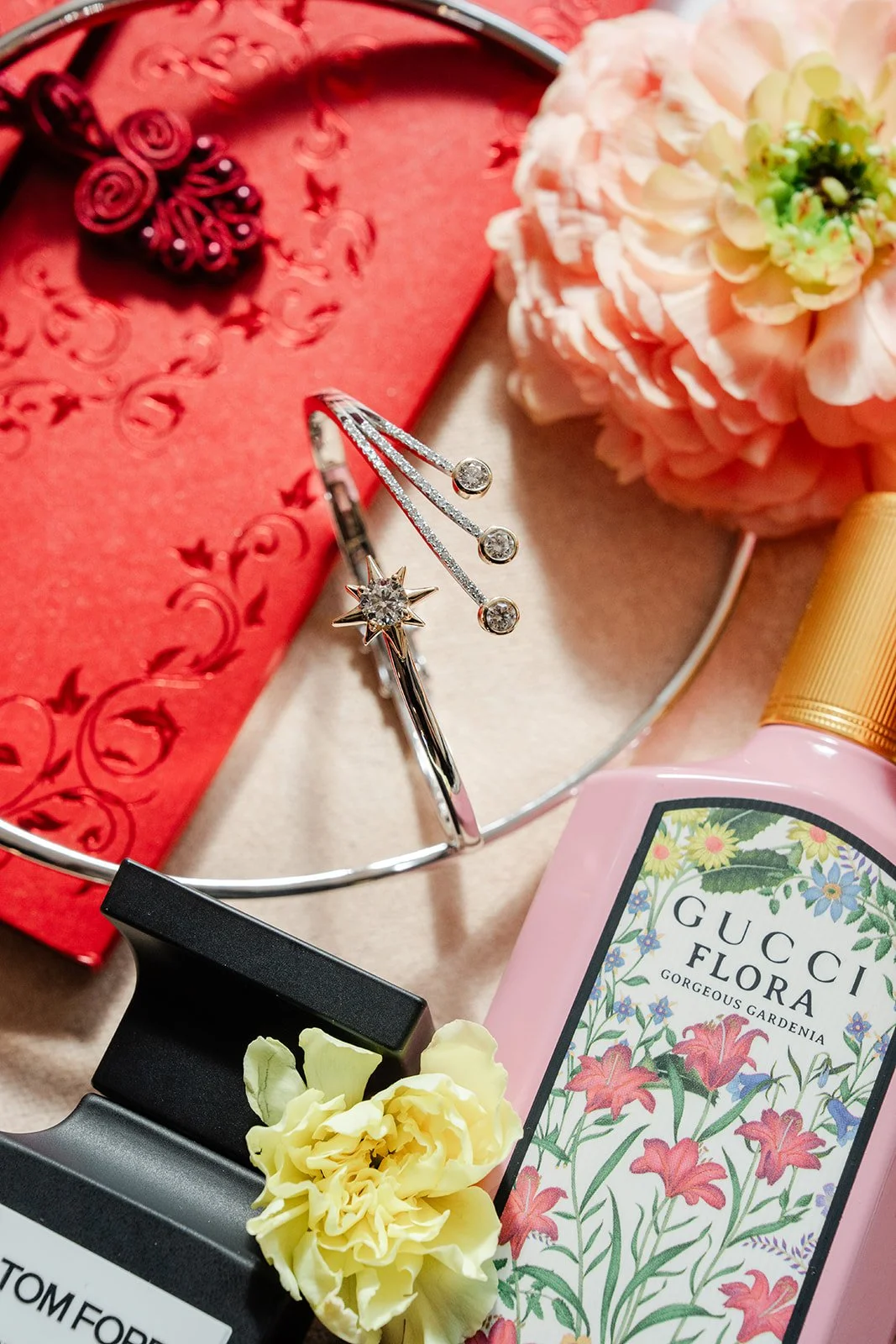 Bridgette's flat lay with a red embroidered clutch, peach roses, perfume and jewelry.