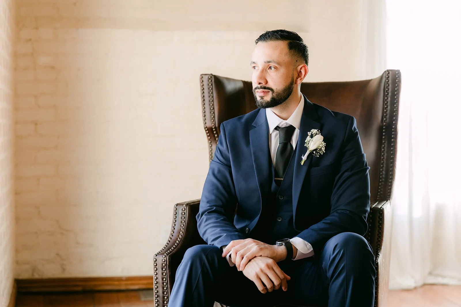 Danny in his navy suit and white boutonniere in the leather chair