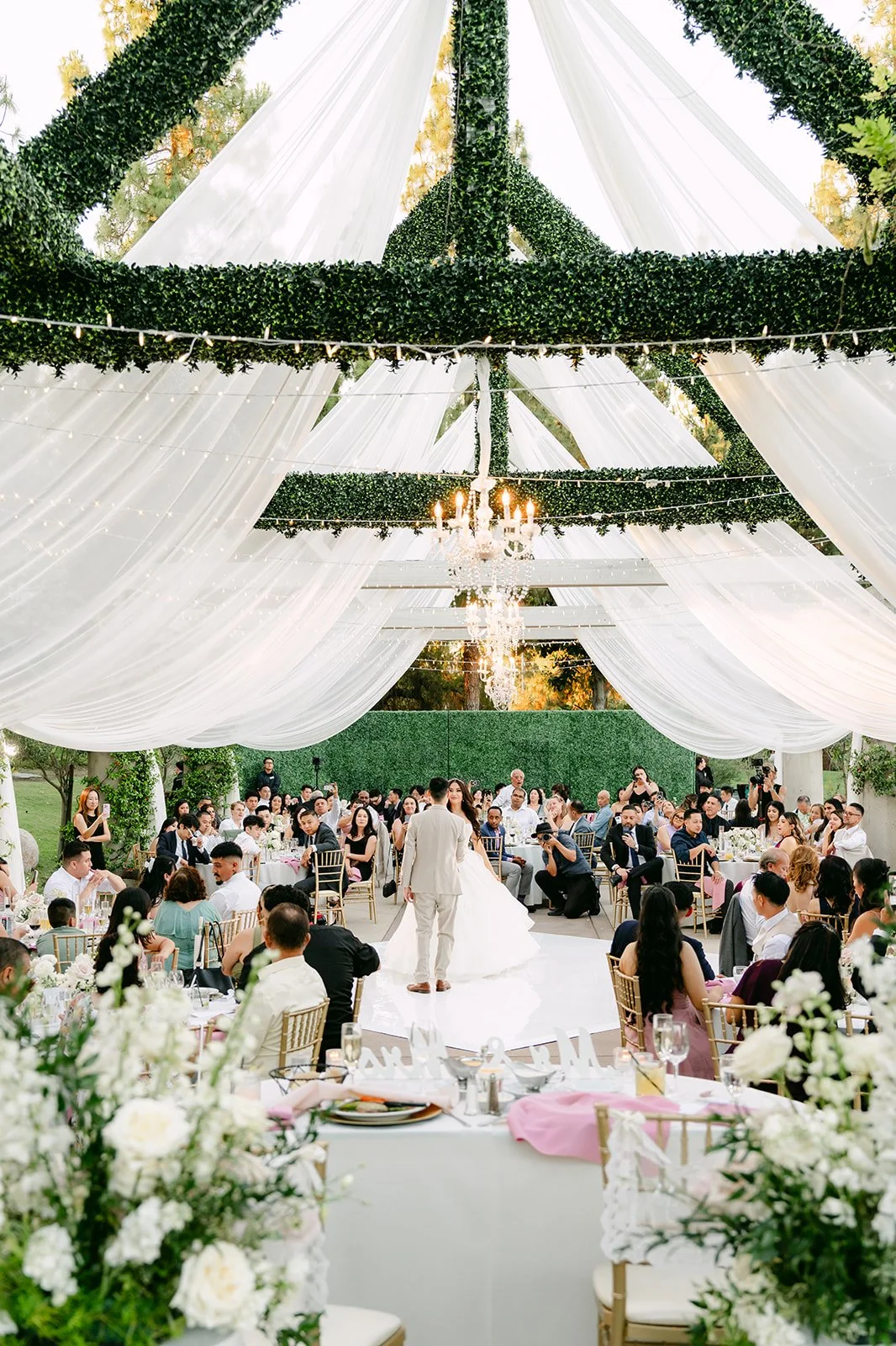 Wide view of Sandra and Kevin's first dance under the draped pergola and chandeliers.