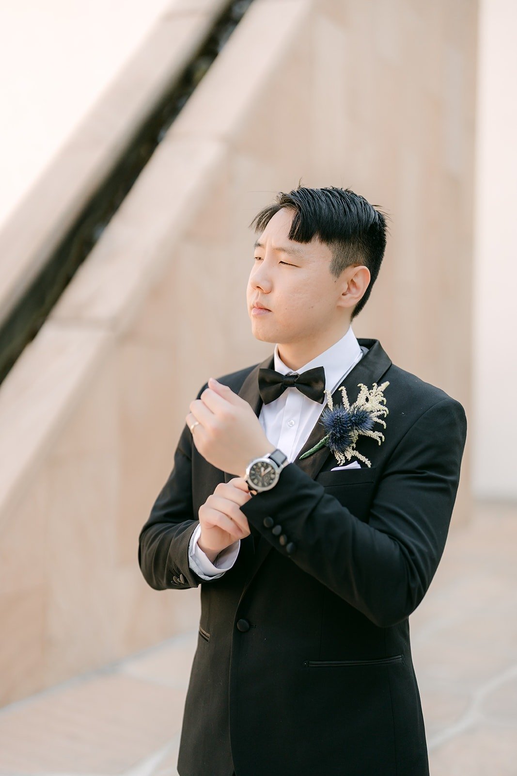 James adjusting his cufflink, blue thistle boutonniere on his lapel