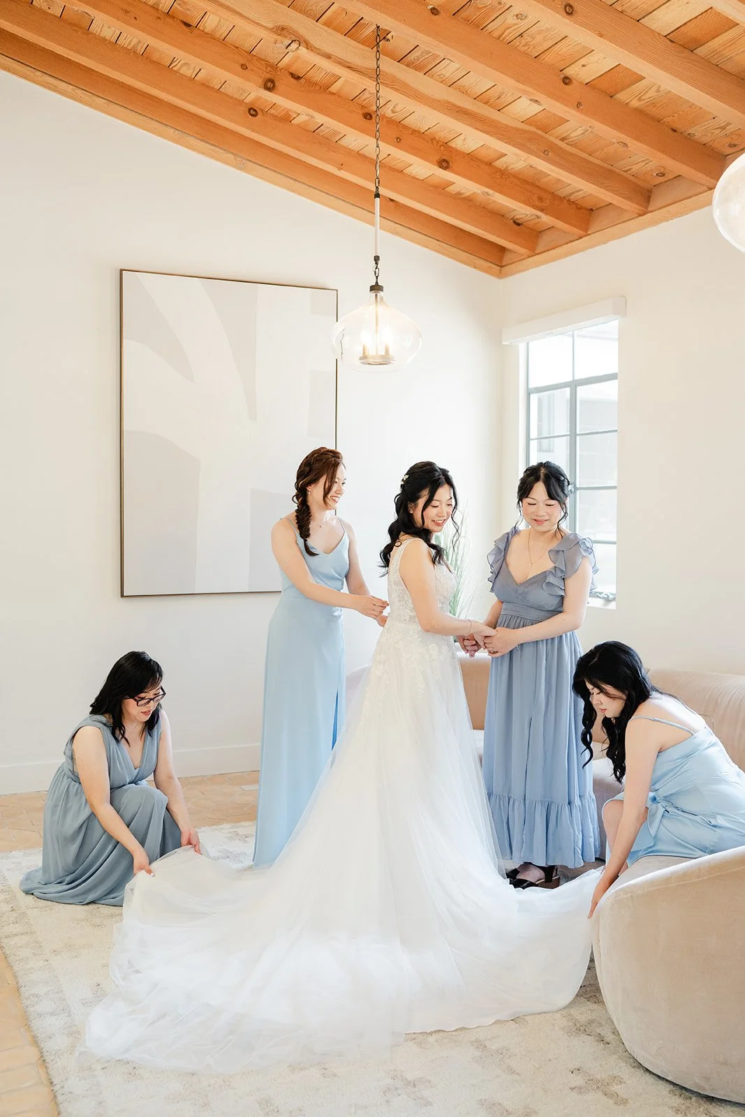 Bridesmaids in dusty blue fluffing the bride's train under the wood beam ceiling