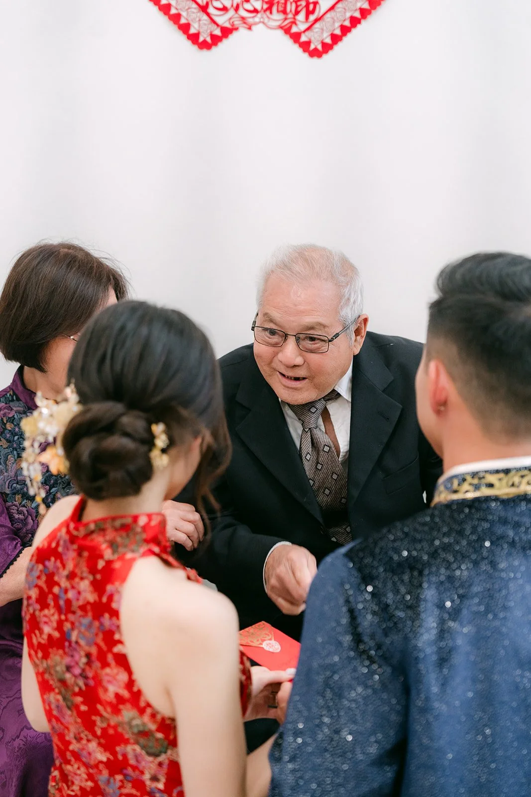 A bride and groom serving tea to an elder under red decorations.