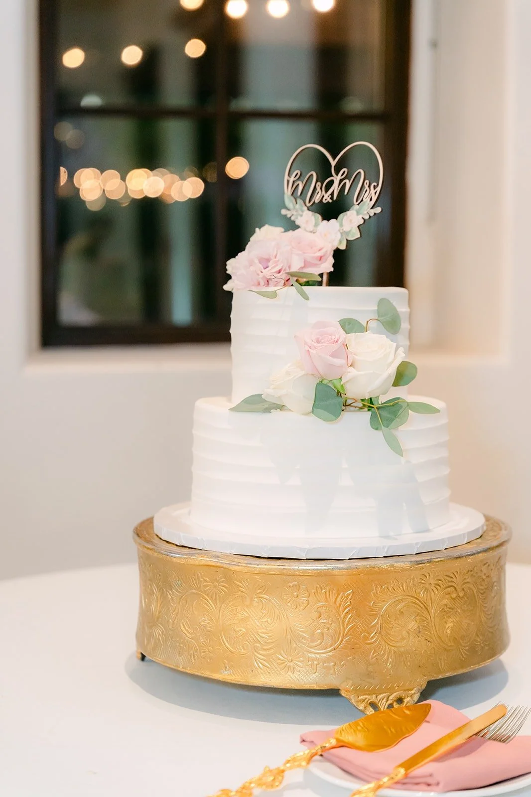 Three tier white cake on a gold stand with pink roses