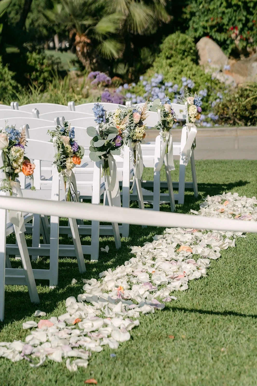 The petal aisle and white chairs on the ceremony lawn, photographed by One and Only Production