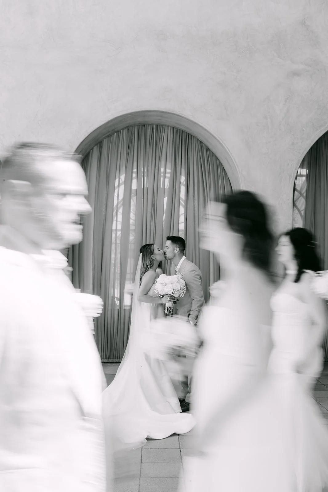 Black and white motion blur of the wedding party walking past the couple