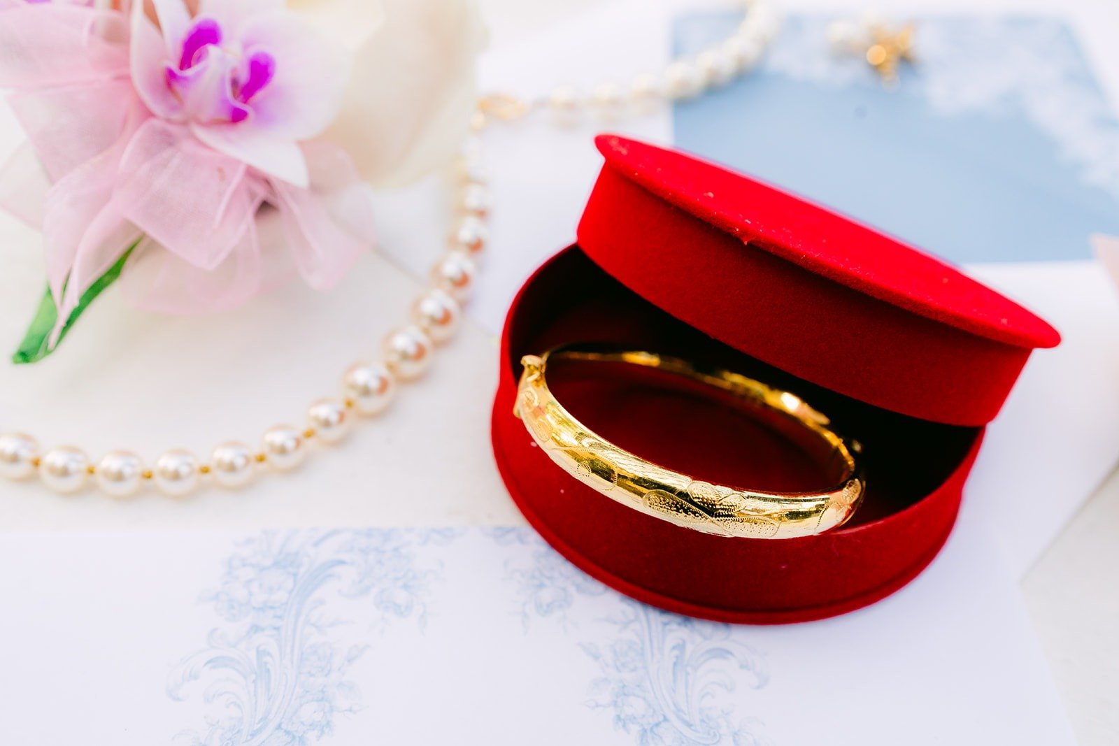 Gold bangle in a red jewelry box beside a pearl necklace