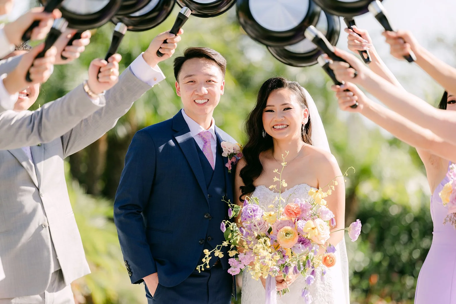 The wedding party holding frying pans over Vannie and Elijah.