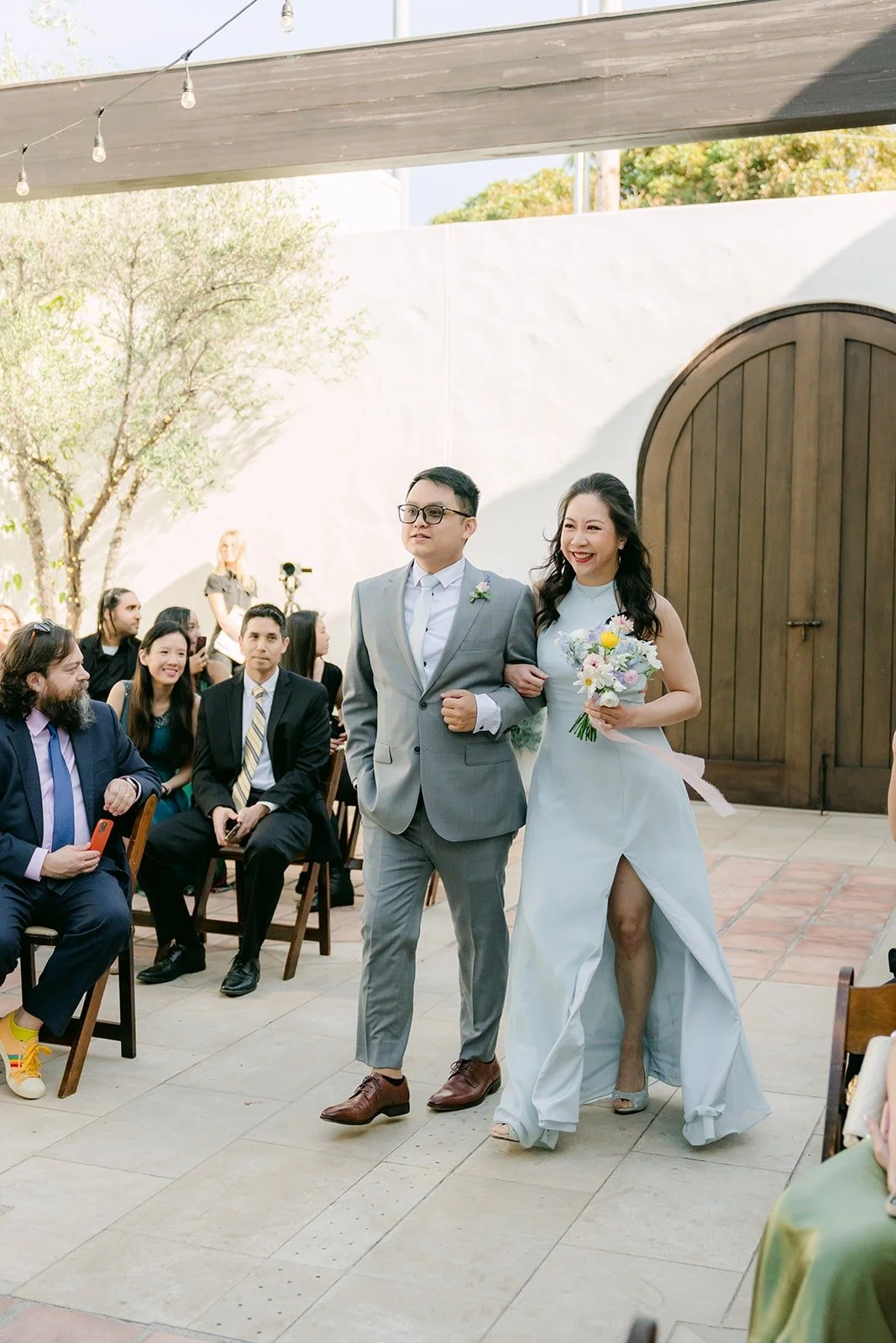 A groomsman and bridesmaid walking in the processional, guests seated along the courtyard