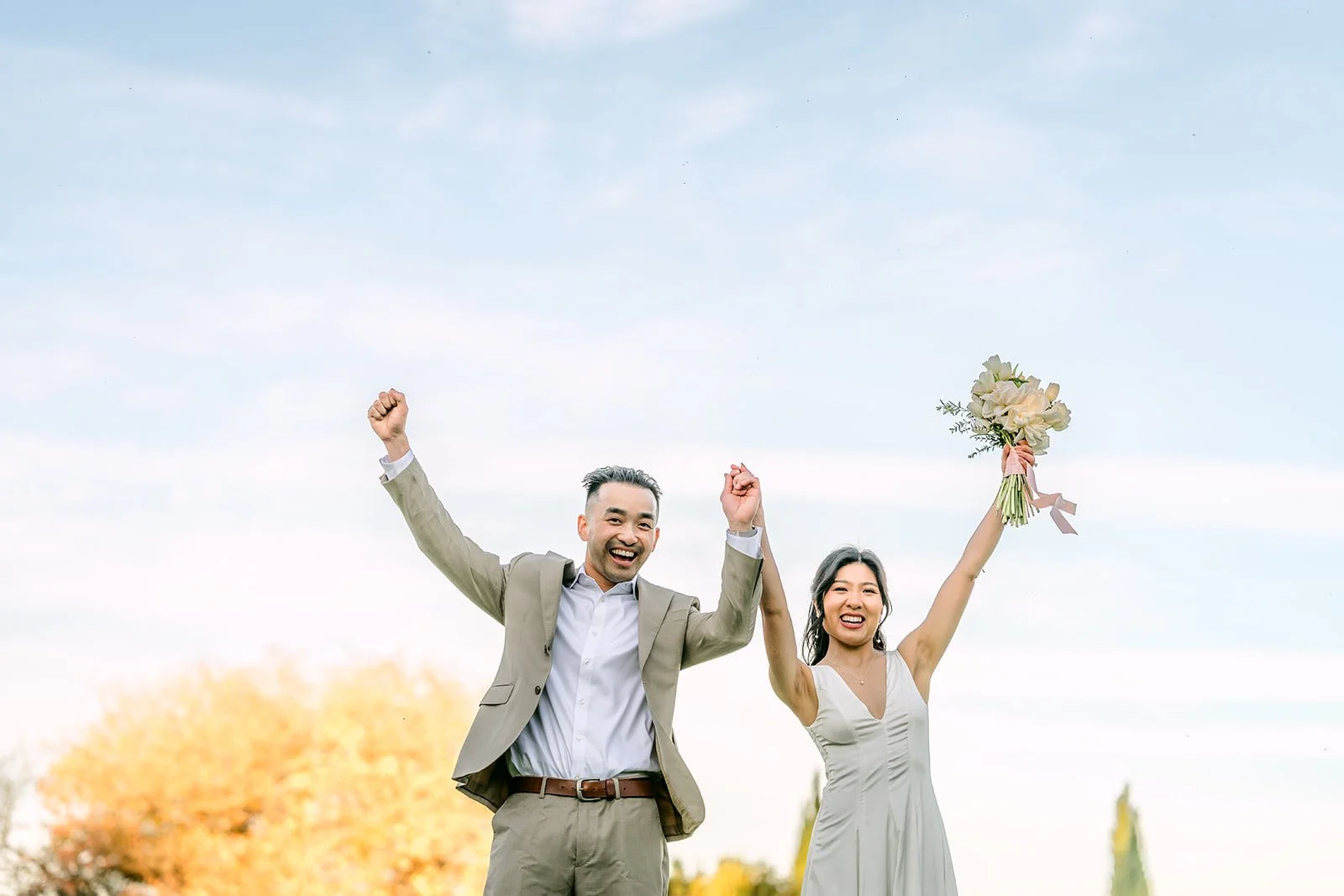Kim and Vincent cheering with the bouquet raised on the meadow.