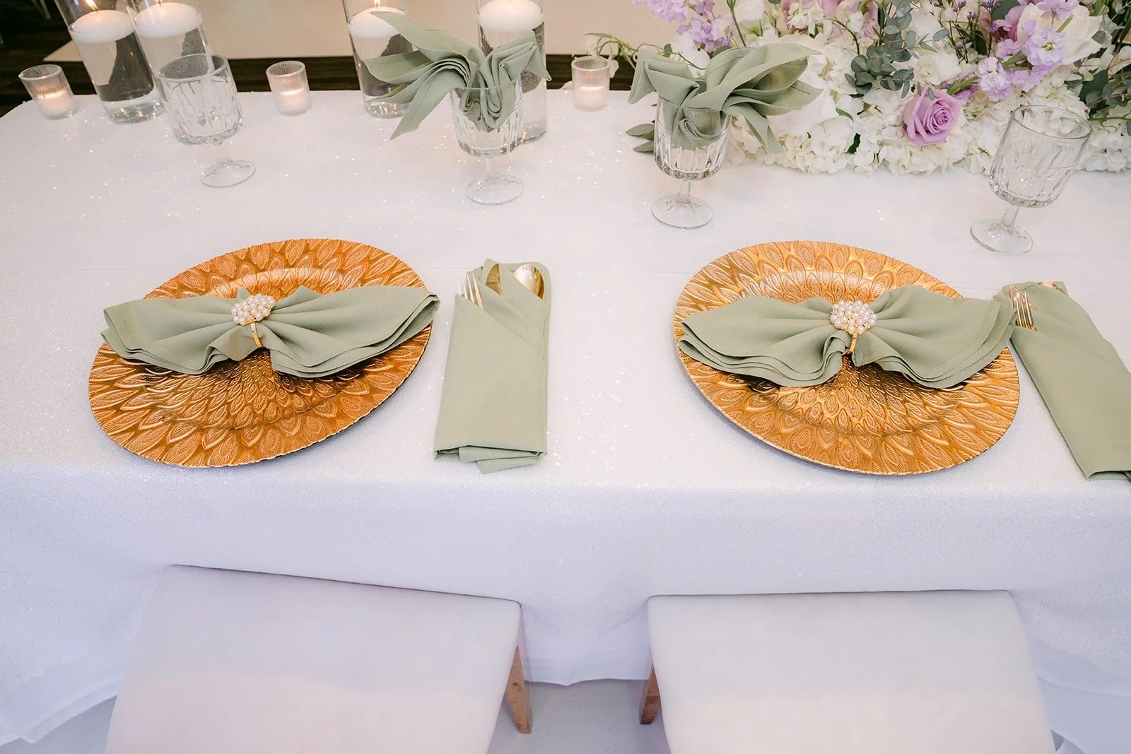 Rattan chargers and sage napkins on a white linen table setting