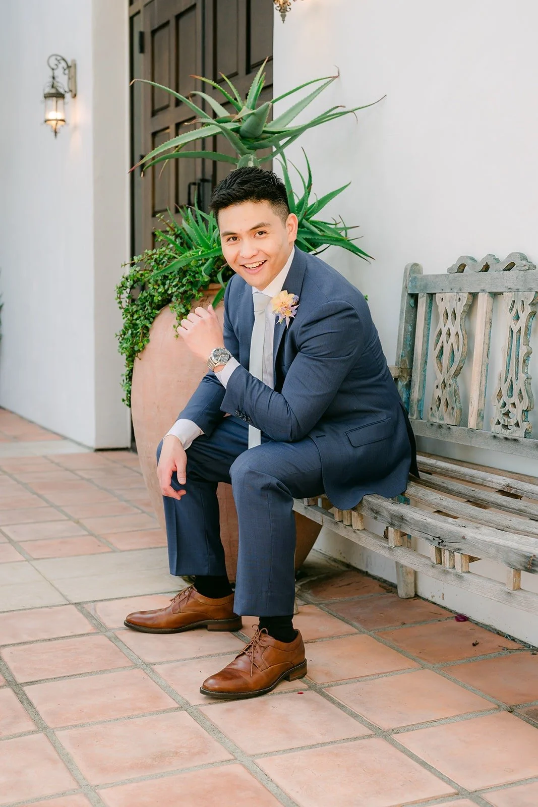 Jerrick sitting on a courtyard bench beside the potted plants