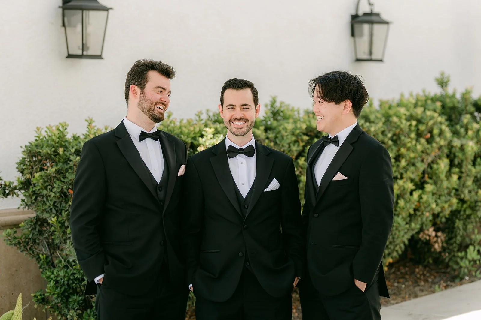 Kevin laughing with two of his groomsmen in black tuxedos