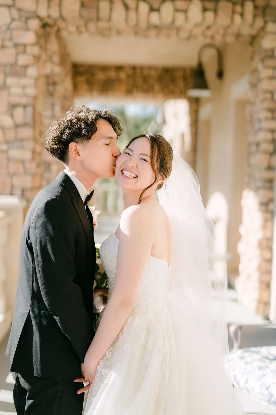 Groom kissing the bride's cheek on the terrace at Vellano Estate
