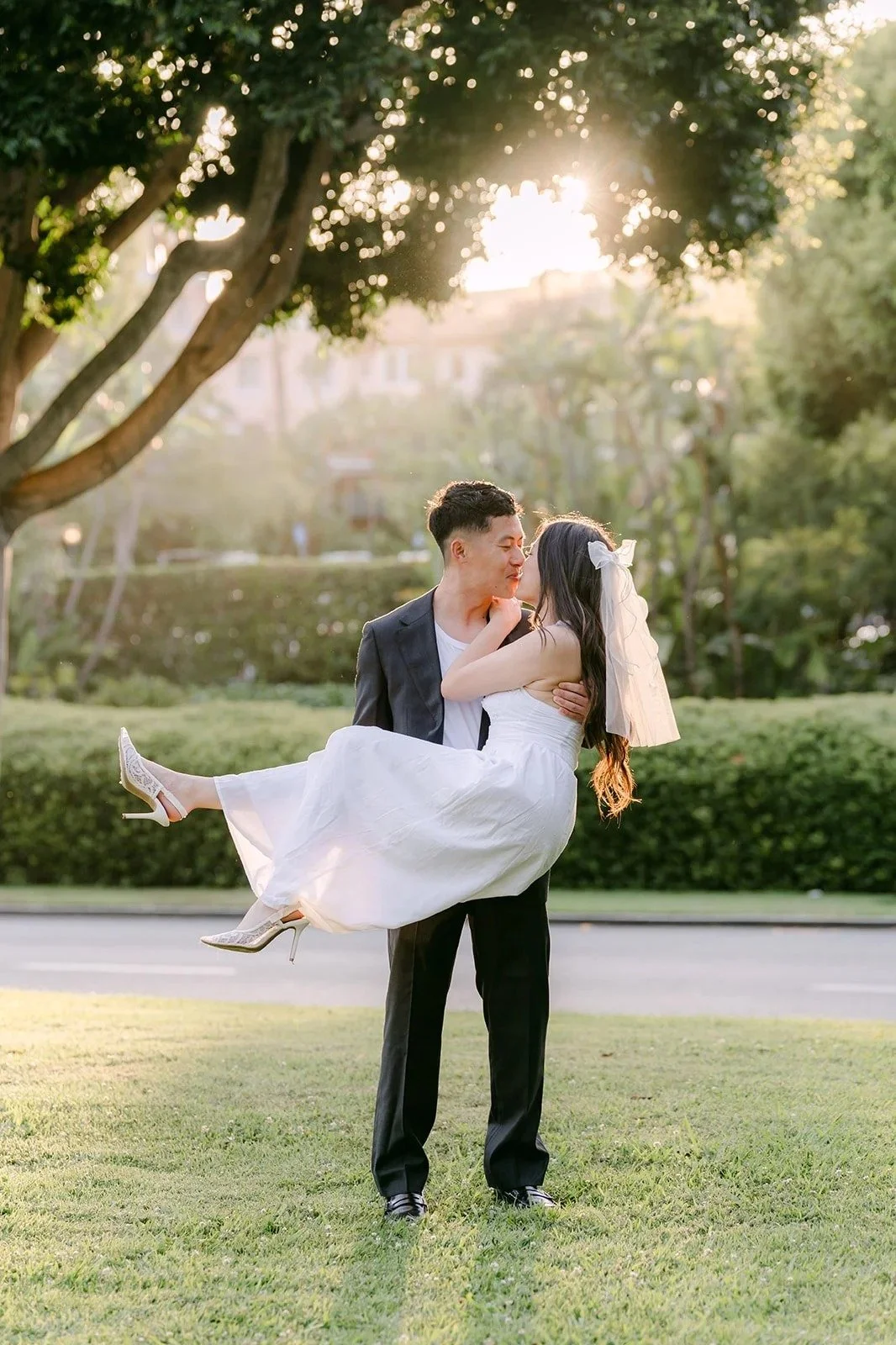 Richard carries Jadee in his arms on the lawn under the trees at golden hour.