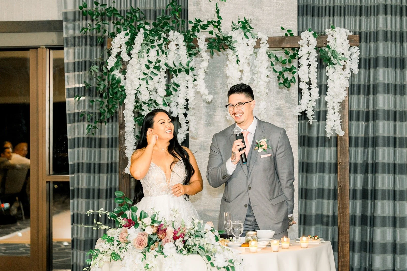 Betsy and Mikey at the sweetheart table under the hanging florals
