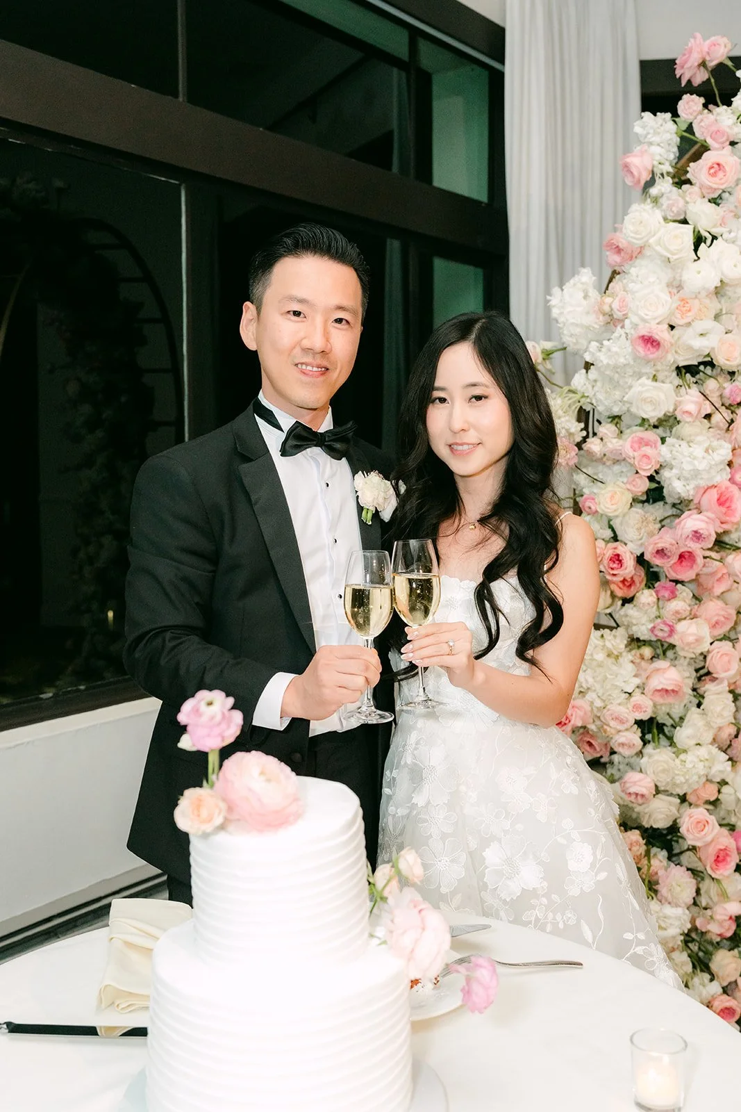 Kelley and Kai raising champagne beside the wedding cake
