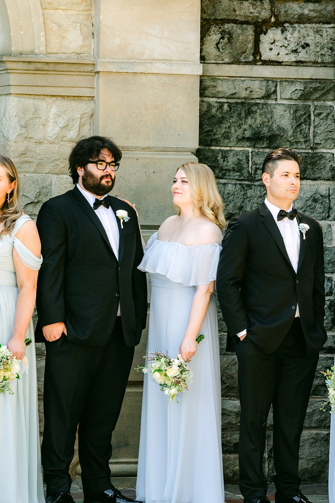 Bridesmaids and groomsmen paired up against the stone wall