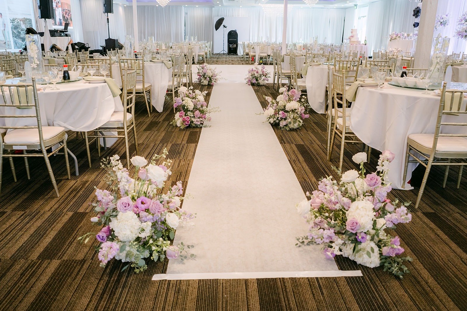 A white aisle runner lined with lavender and white florals between the guest tables