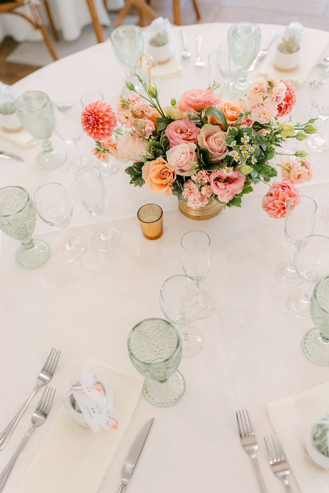 A centerpiece of peach and pink roses on a white linen table