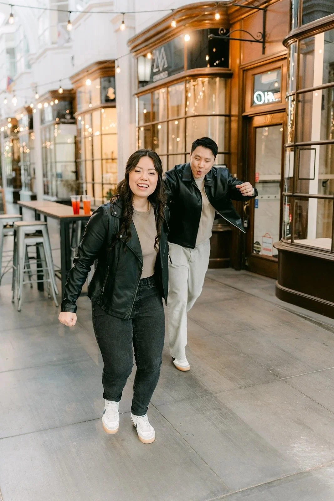 Emily and James walk through the Burlington Arcade in matching leather jackets.