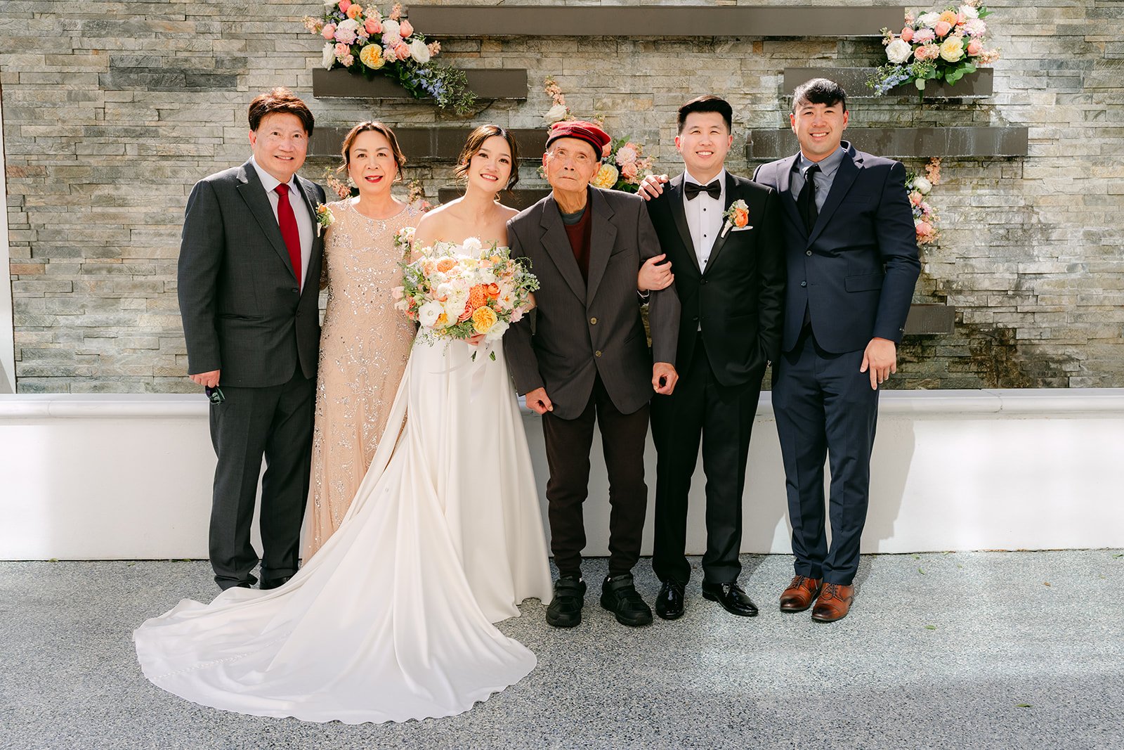 Amanda and San with family in front of the stone wall.