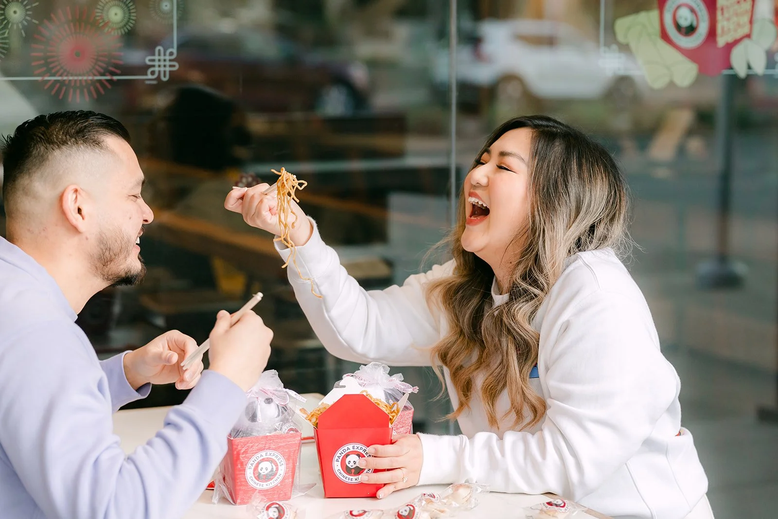 Linh laughs as Ankush feeds her a bite with chopsticks.