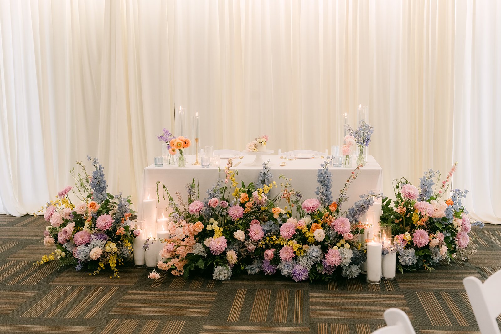Pastel florals lining the sweetheart table in front of white drapes.
