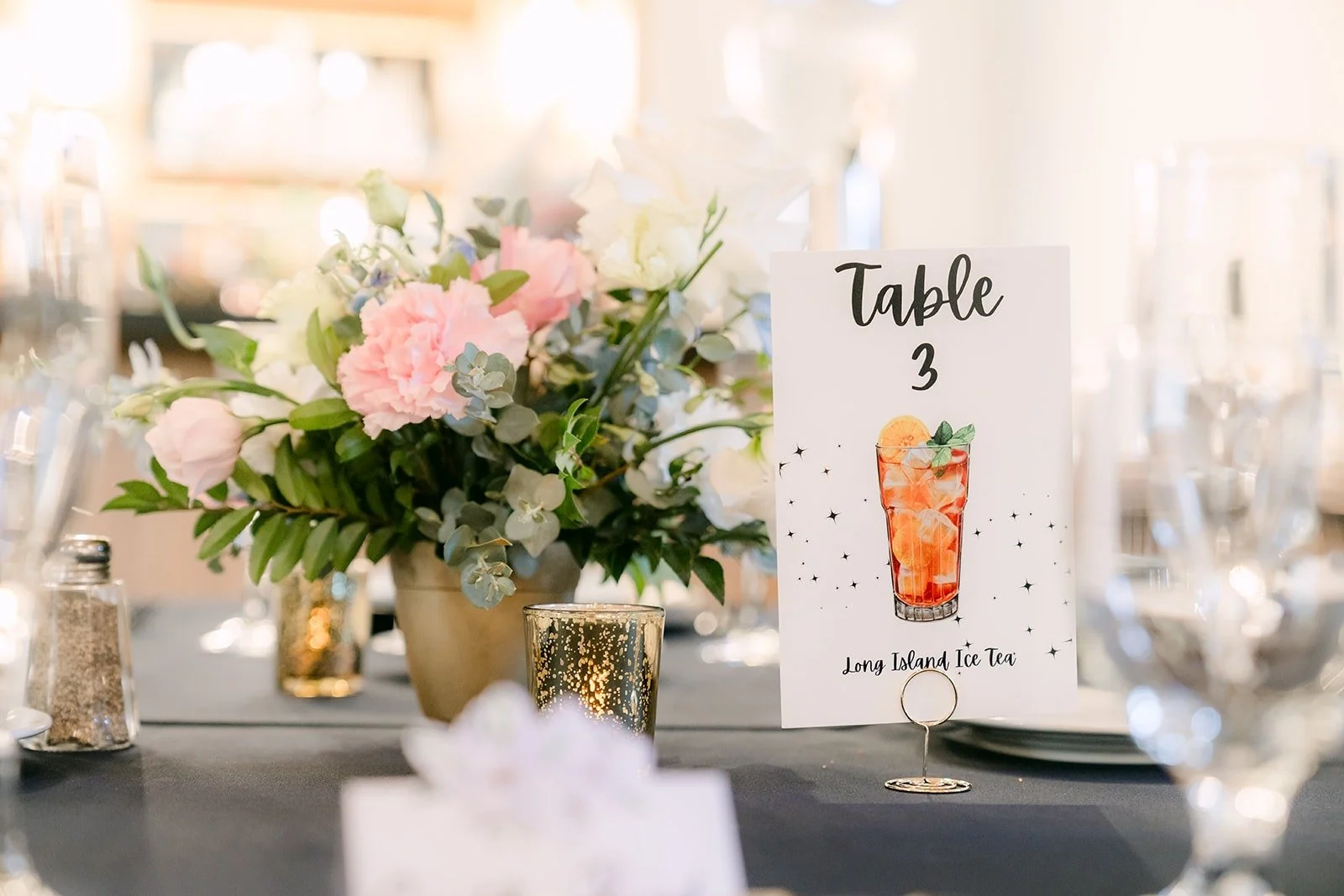 A table number card with a drink illustration beside blush and white florals