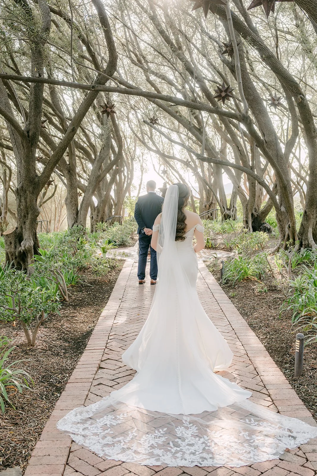 Mariana walking down the brick path through the olive grove toward Danny for their first look