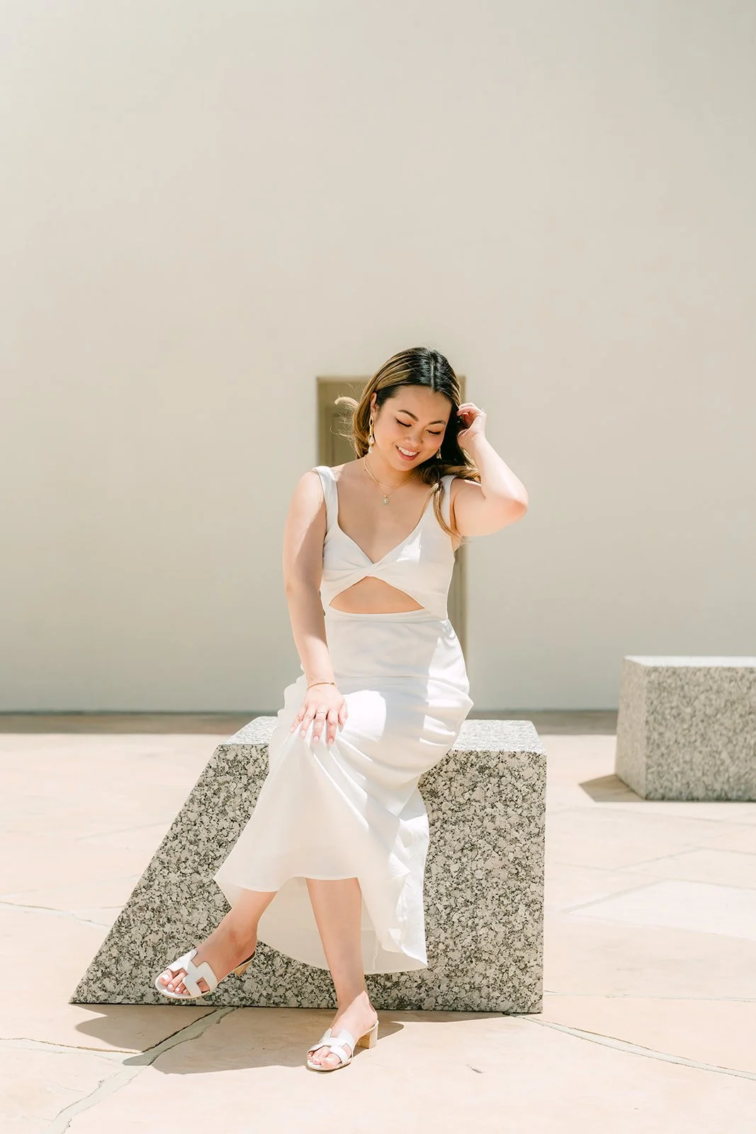 Stephanie seated on a granite block in her white two-piece outfit.