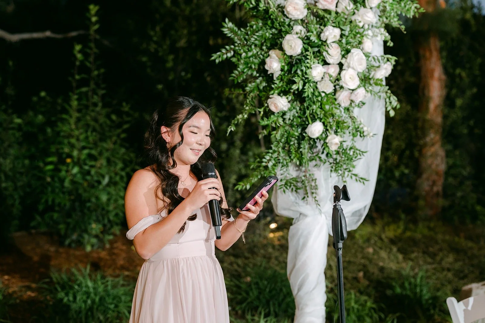 A bridesmaid giving a toast beside the floral arch under the evening lights