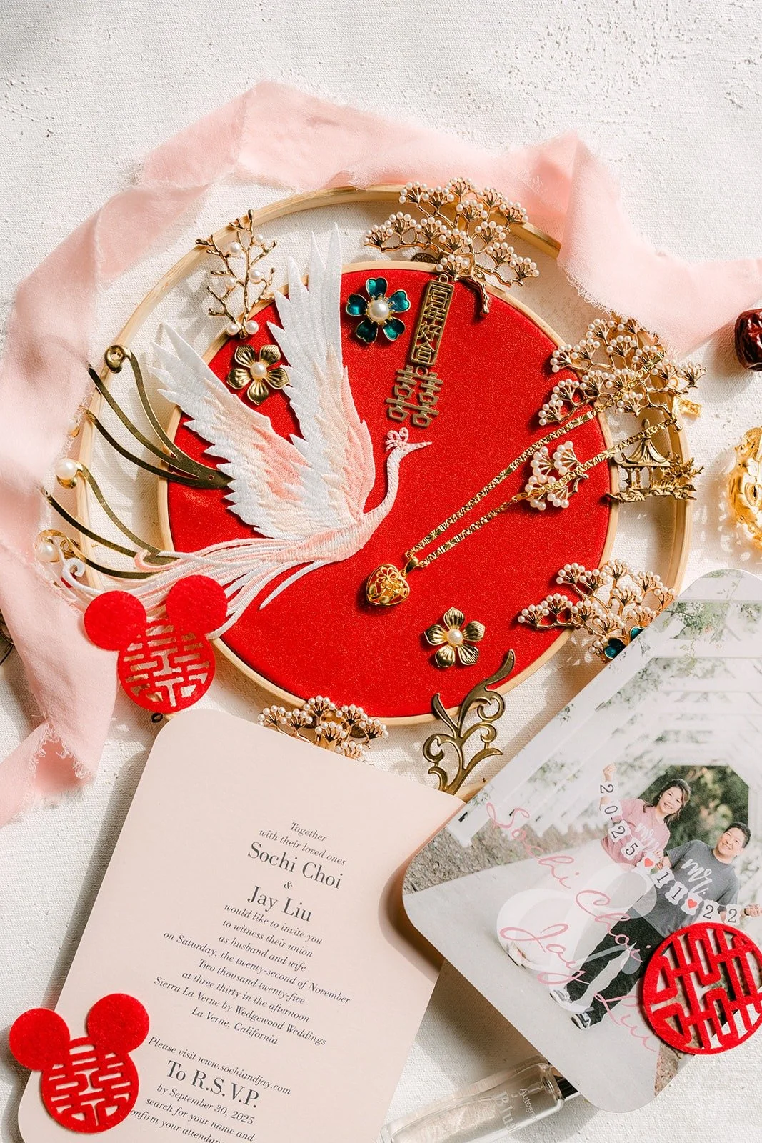 Gold Chinese wedding jewelry and hair pieces arranged on a red fan beside the invitation