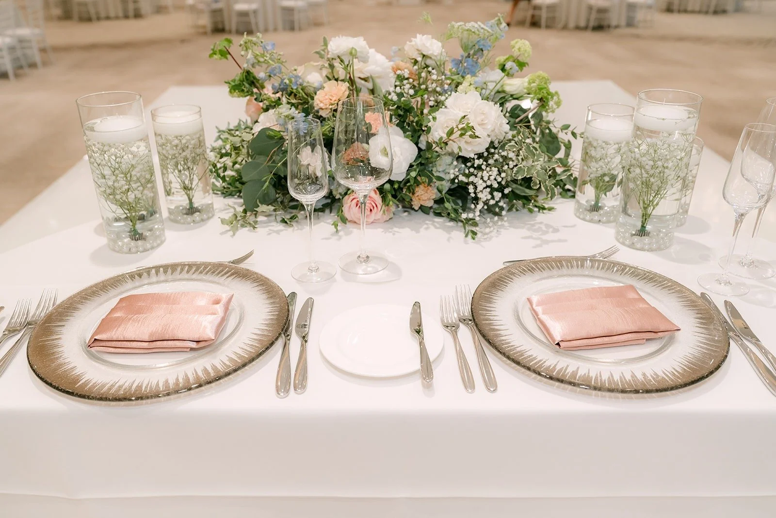 Centerpiece of white roses, blush blooms and greenery over gold chargers