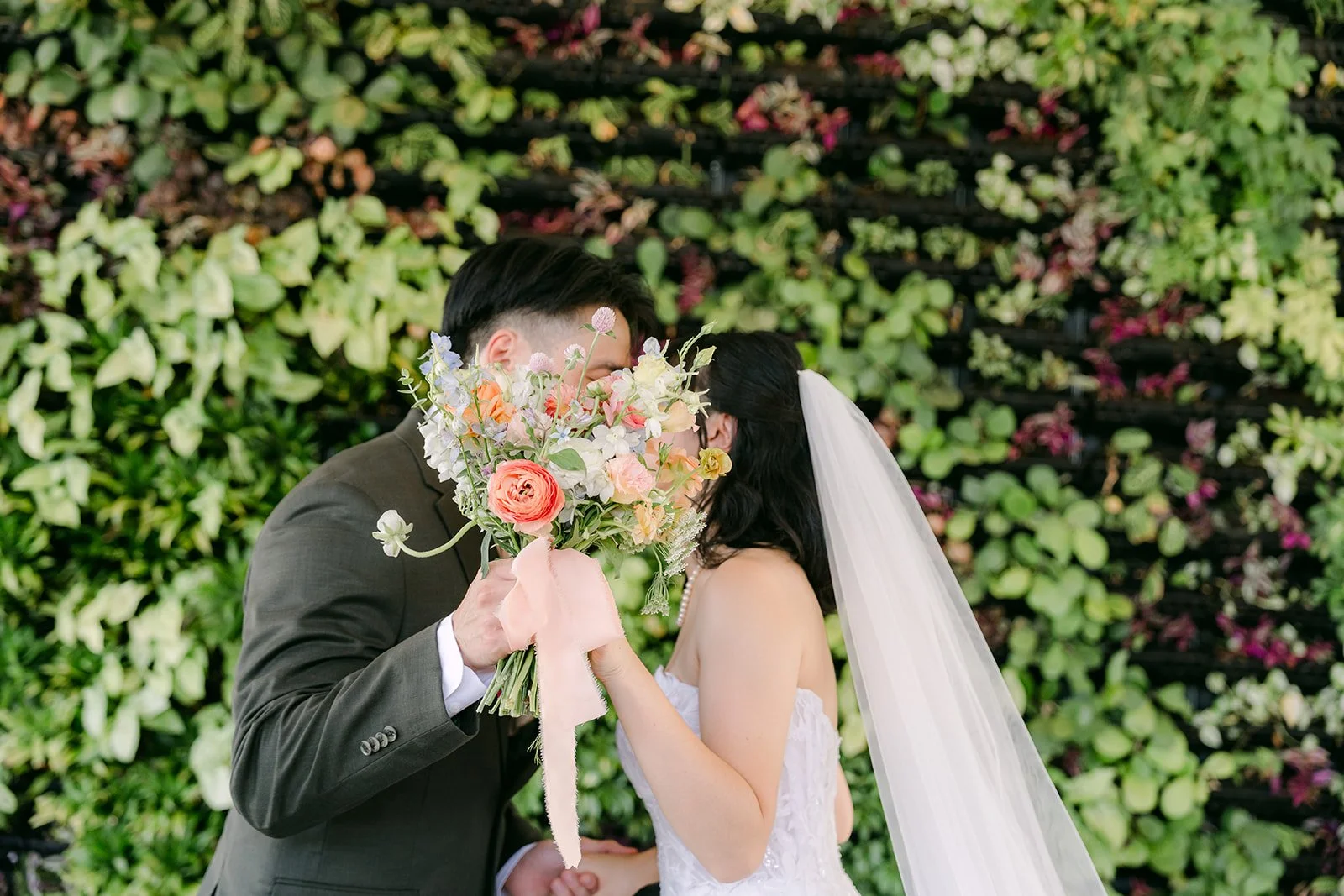 Couple kissing behind Vivian's bouquet at the Colony House living wall
