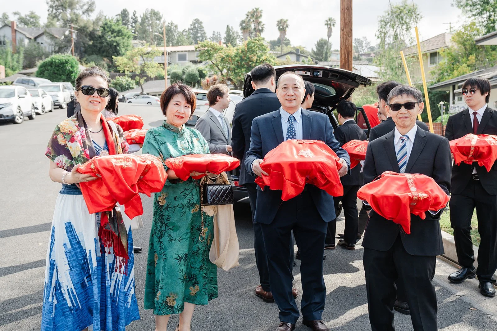 The groom's family walking up the street carrying red covered gift trays.